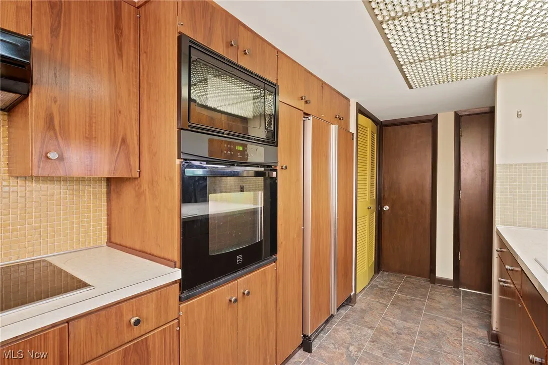 Kitchen with backsplash, light countertops, black appliances, brown cabinetry, and ventilation hood