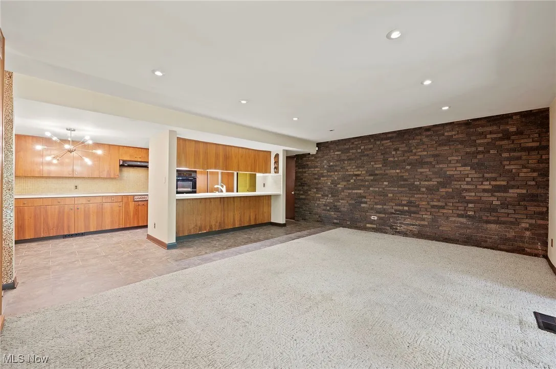 Unfurnished living room featuring light colored carpet, brick wall, recessed lighting, and a chandelier
