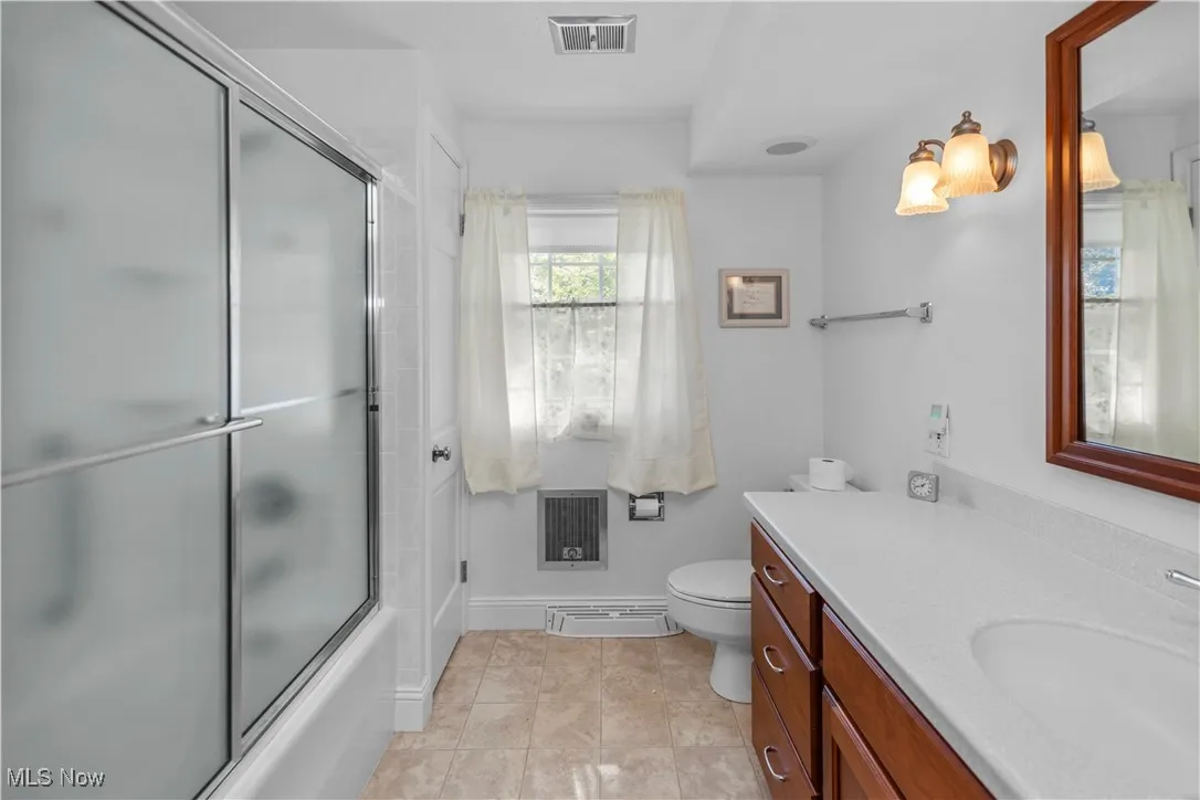 Full bathroom featuring vanity, bath / shower combo with glass door, light tile patterned floors, and heating unit
