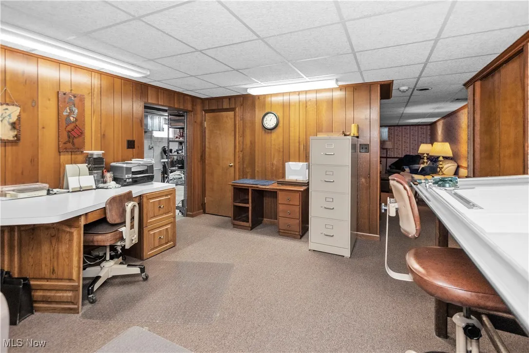 Office area featuring a paneled ceiling, wood walls, and light colored carpet