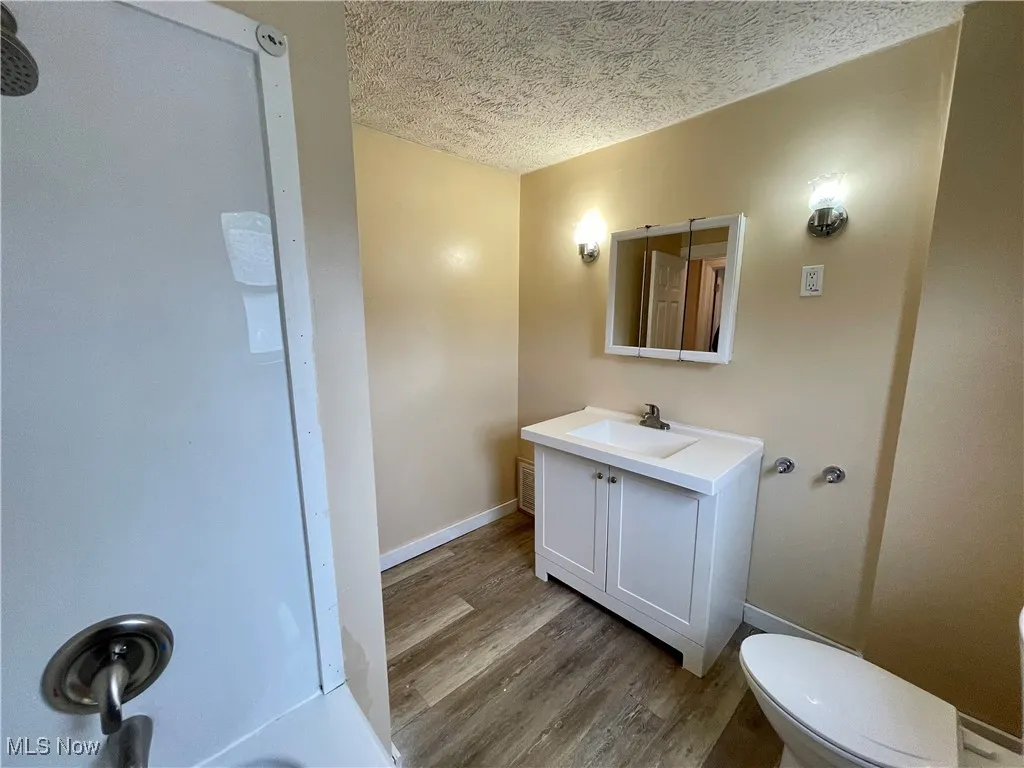 Full bathroom featuring a textured ceiling, vanity, and light wood finished floors