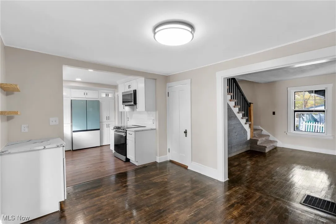 Kitchen featuring light stone counters, appliances with stainless steel finishes, white cabinets, backsplash, and dark wood finished floors