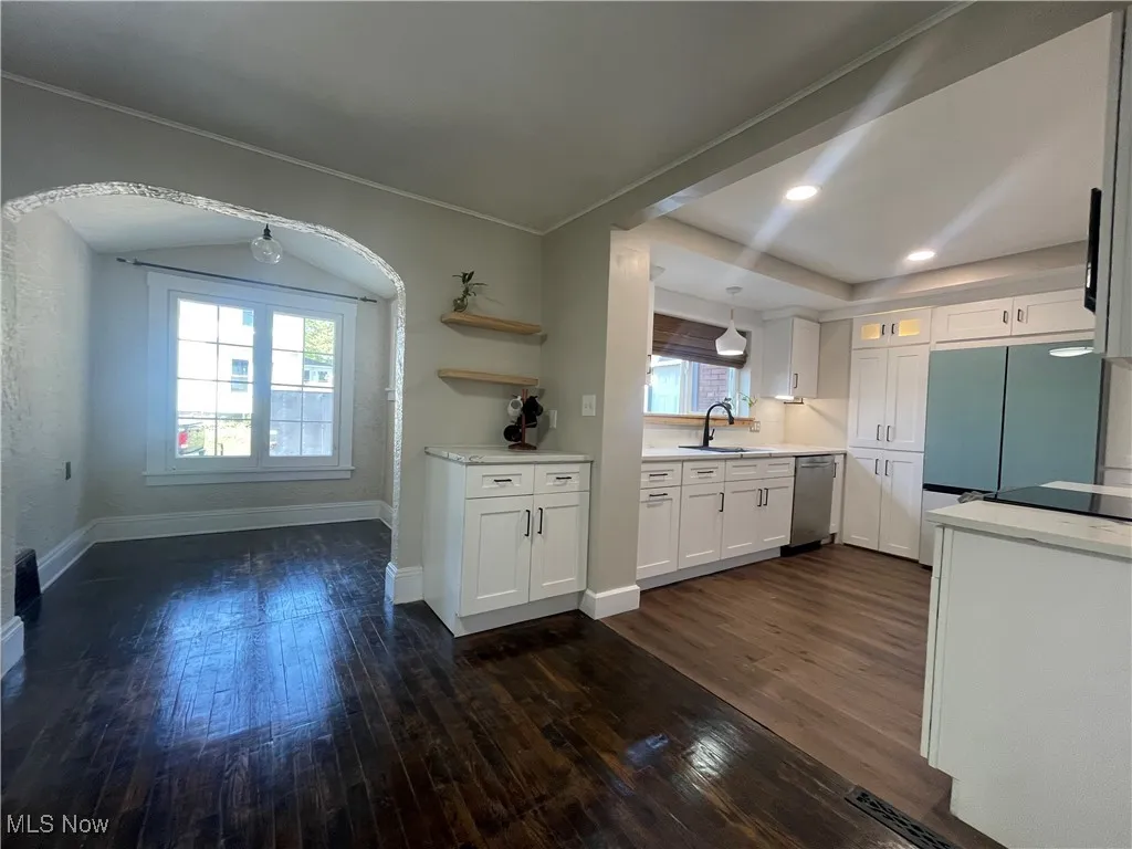Kitchen with white cabinetry, glass insert cabinets, dark wood-type flooring, freestanding refrigerator, and stainless steel dishwasher