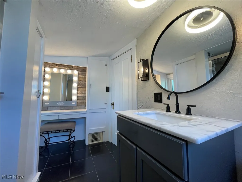 Bathroom with a textured ceiling, dark tile patterned flooring, vanity, and a textured wall