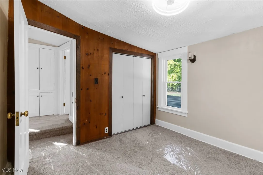 Unfurnished bedroom with carpet, wooden walls, vaulted ceiling, a textured ceiling, and a closet