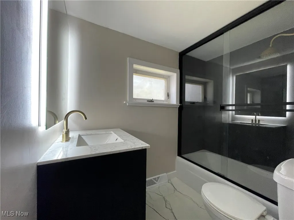 Bathroom with vanity, enclosed tub / shower combo, and light marble finish flooring
