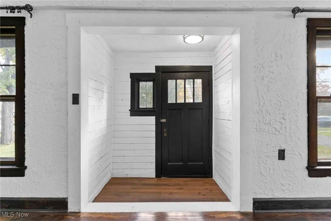 Foyer entrance with a textured wall, plenty of natural light, dark wood-style floors, and wood walls