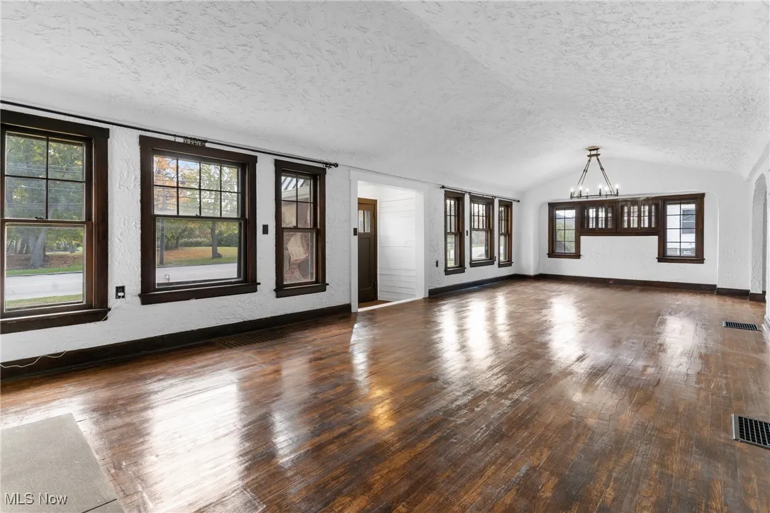Unfurnished living room with a textured wall, dark wood-style flooring, lofted ceiling, a textured ceiling, and a chandelier