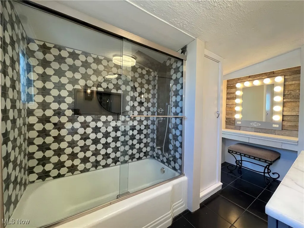Bathroom featuring shower / bath combination with glass door, dark tile patterned flooring, a textured ceiling, lofted ceiling, and vanity