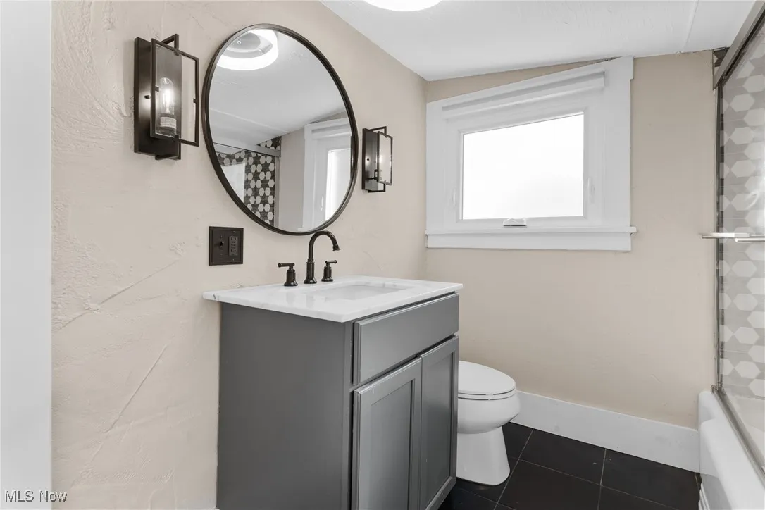 Full bathroom with dark tile patterned floors, vanity, and shower / bath combo with shower curtain