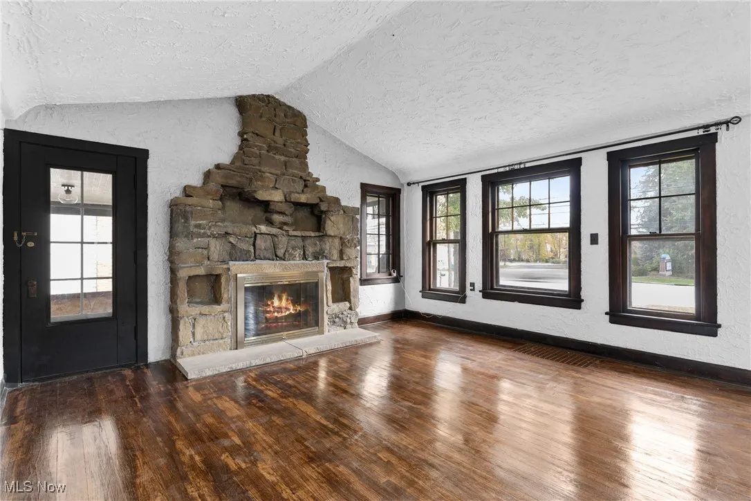 Unfurnished living room with a textured wall, a textured ceiling, wood-type flooring, a stone fireplace, and vaulted ceiling