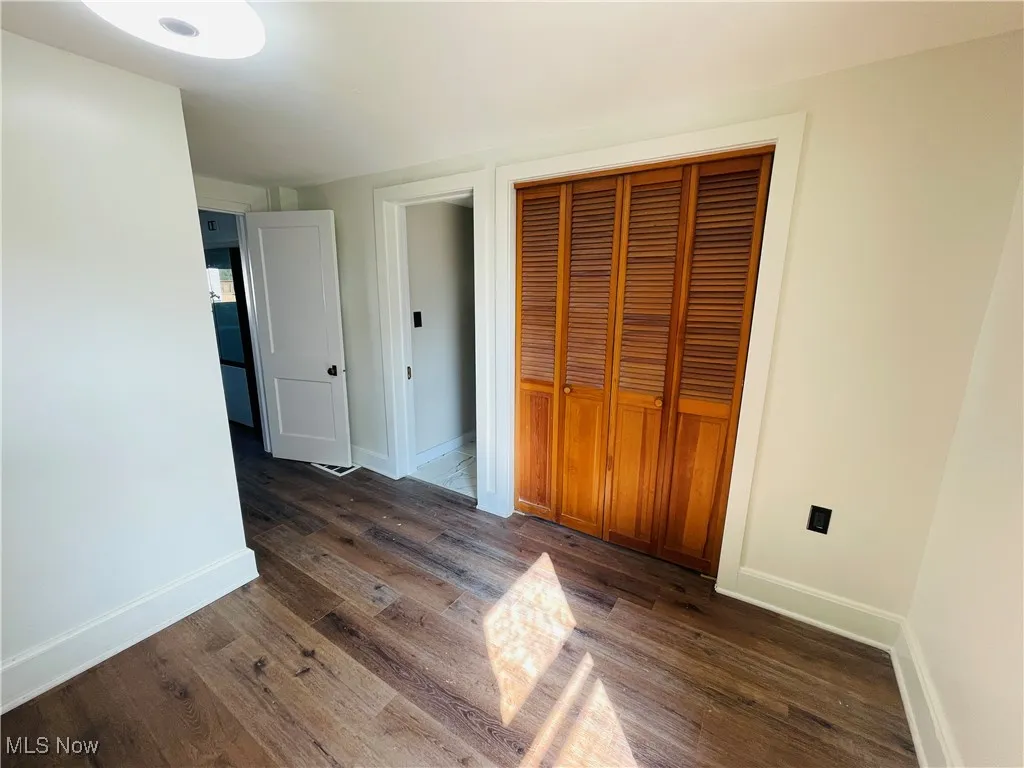 Unfurnished bedroom with dark wood-style floors and a closet