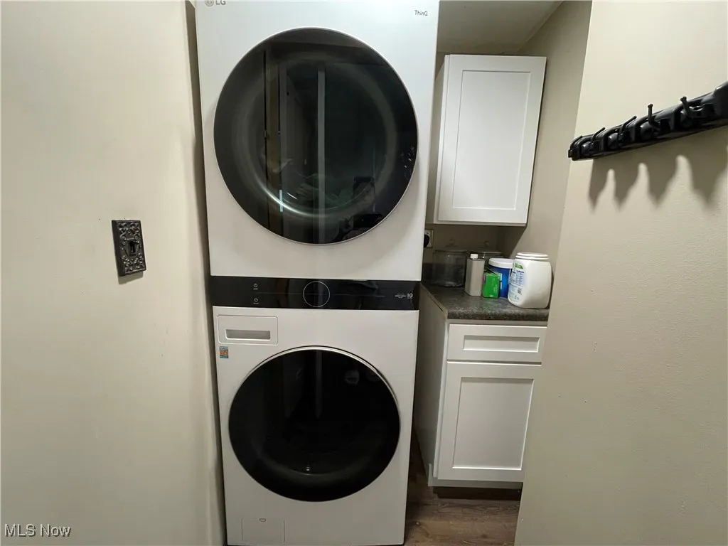 Washroom with stacked washer / drying machine, cabinet space, and dark wood-style flooring