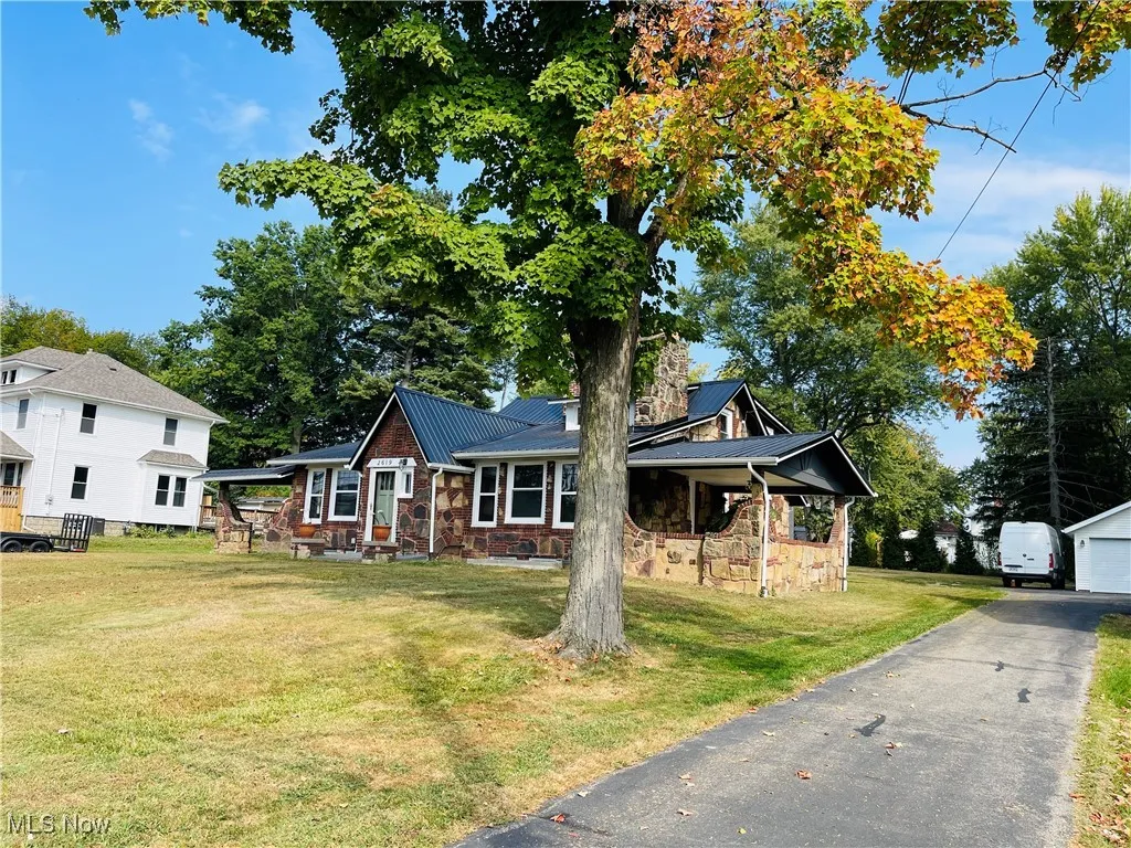 View of front of home with a front yard, a metal roof, a garage, and stone siding