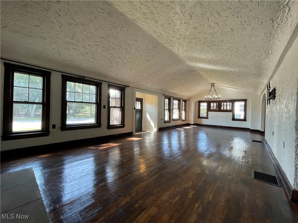 Unfurnished living room featuring a textured wall, lofted ceiling, dark wood-style flooring, a textured ceiling, and a chandelier