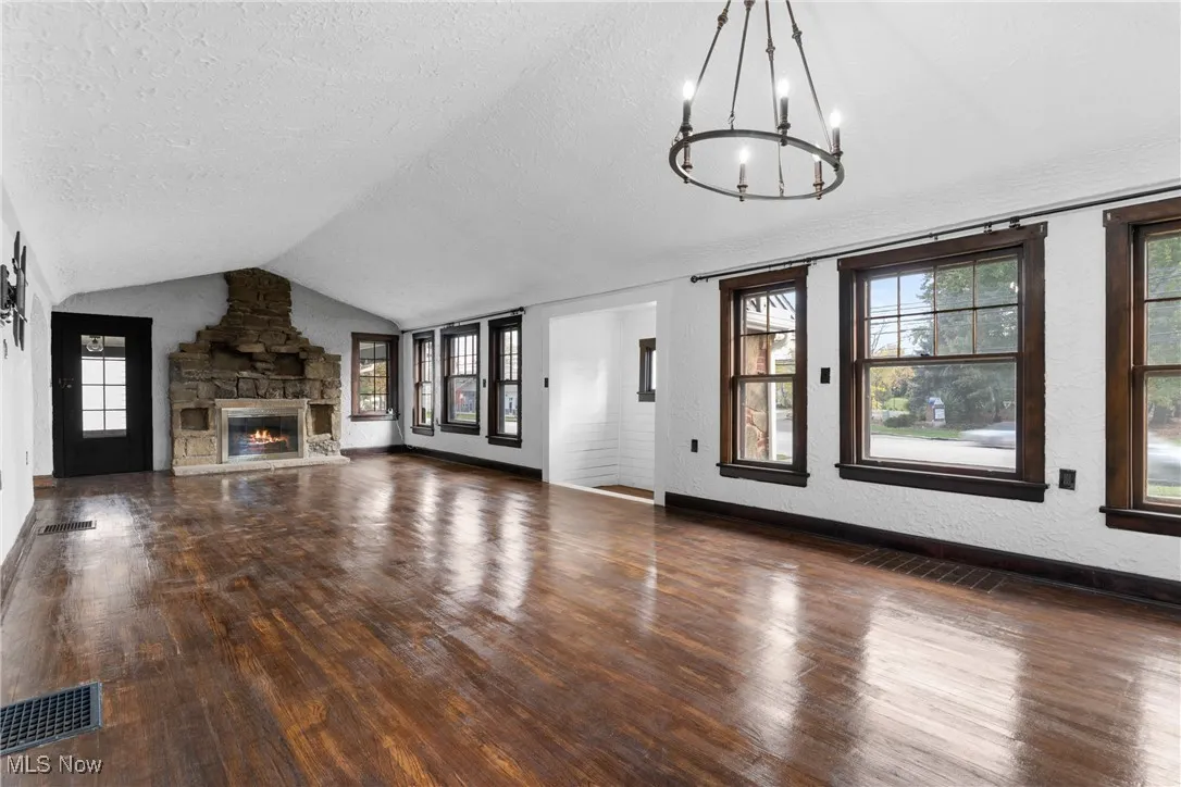 Unfurnished living room with a textured wall, lofted ceiling, dark wood finished floors, a fireplace, and a textured ceiling