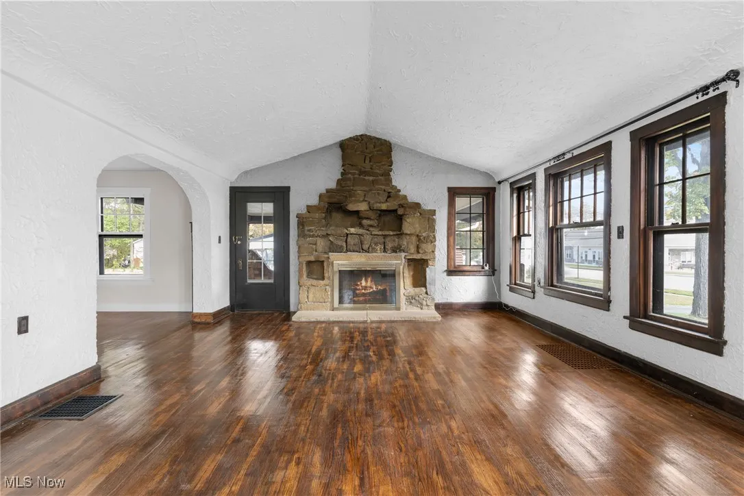 Unfurnished living room featuring a textured wall, dark wood-style flooring, vaulted ceiling, a textured ceiling, and a fireplace
