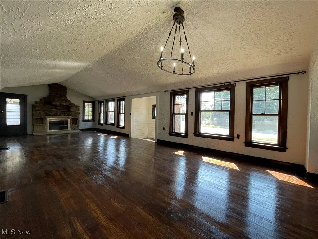 Unfurnished living room featuring lofted ceiling, dark wood-type flooring, plenty of natural light, a textured ceiling, and a chandelier