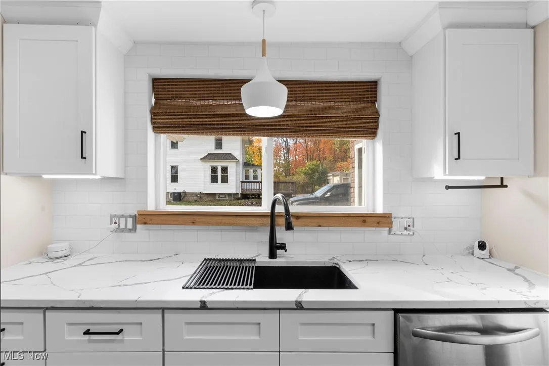 Kitchen featuring light stone counters, dishwasher, white cabinetry, and backsplash