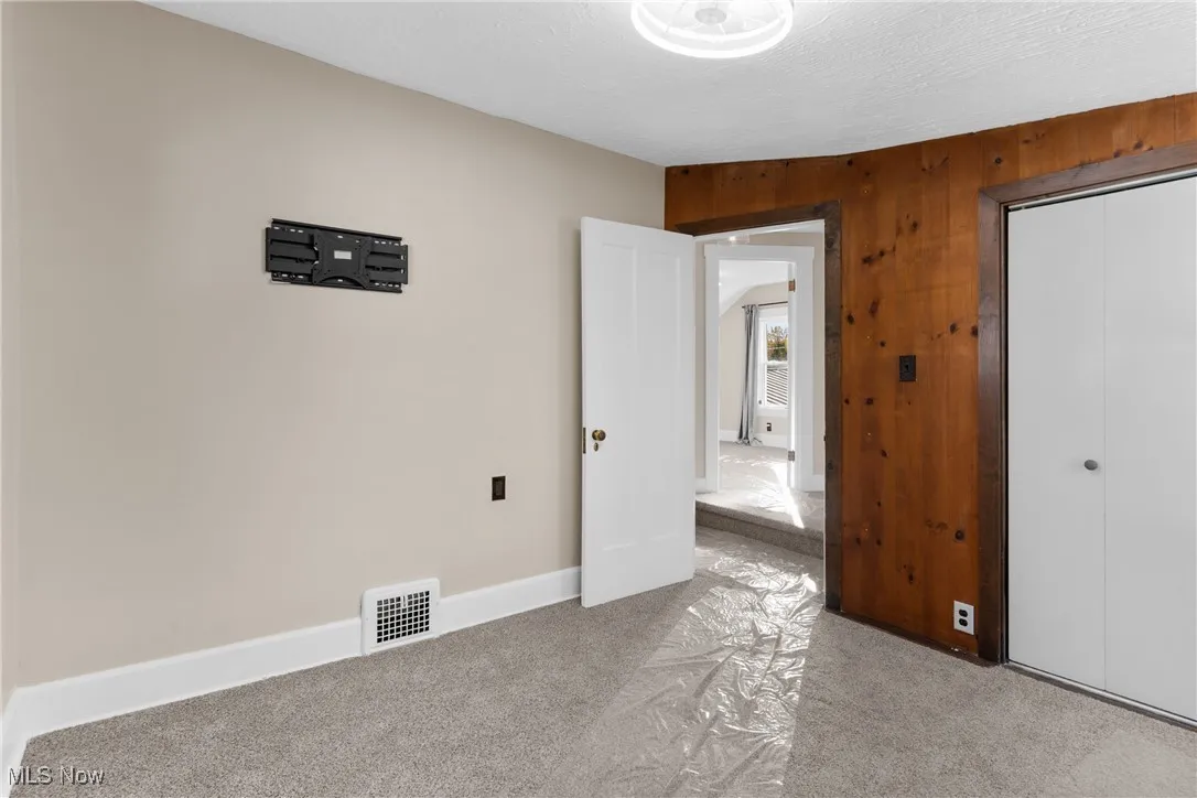 Unfurnished bedroom with carpet floors, wood walls, a textured ceiling, and a closet