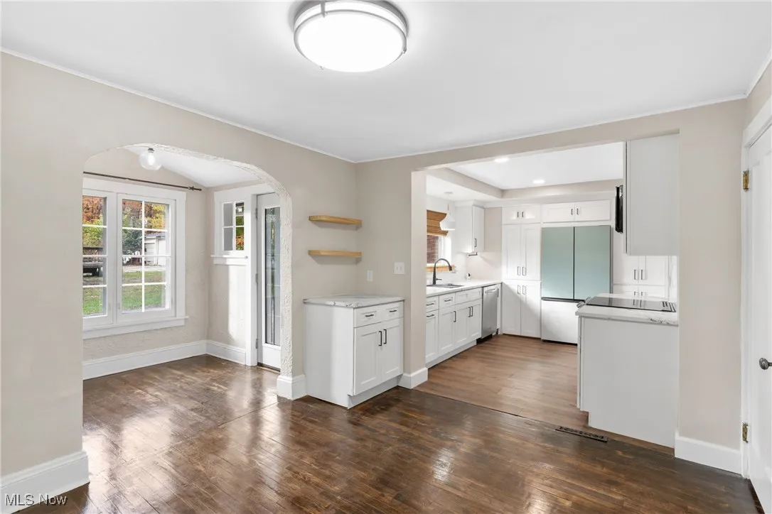 Kitchen with arched walkways, white cabinetry, open shelves, fridge, and dark wood-style floors
