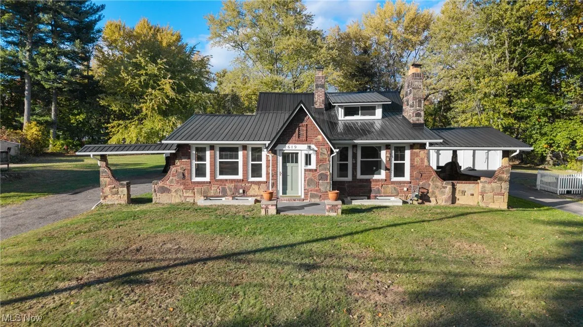 View of front of house featuring a metal roof, a chimney, a front lawn, and view of scattered trees