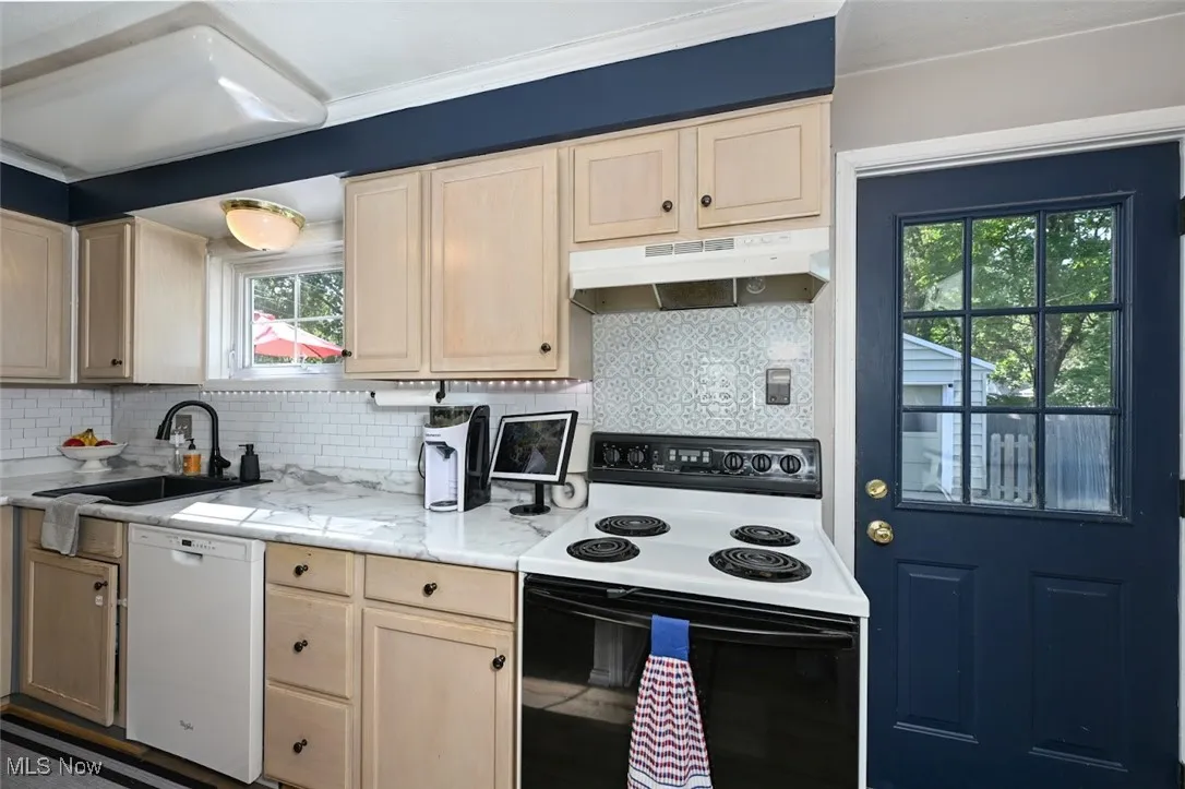 Kitchen with white appliances, light brown cabinets, decorative backsplash, and under cabinet range hood