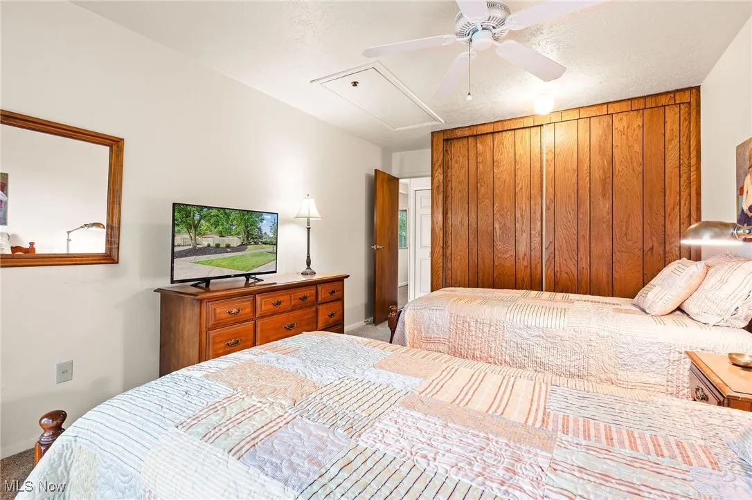 Bedroom with attic access, carpet, wood closet doors, and a ceiling fan