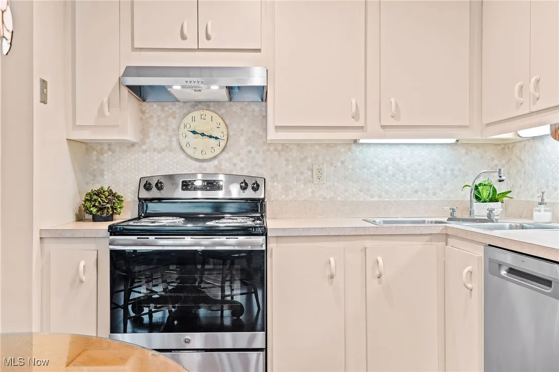 Kitchen featuring appliances with stainless steel finishes, decorative backsplash, light countertops, and under cabinet range hood