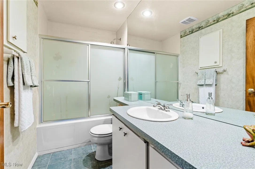Full main bath featuring vanity, bath / shower combo with glass door, recessed lighting, and dark tile patterned flooring