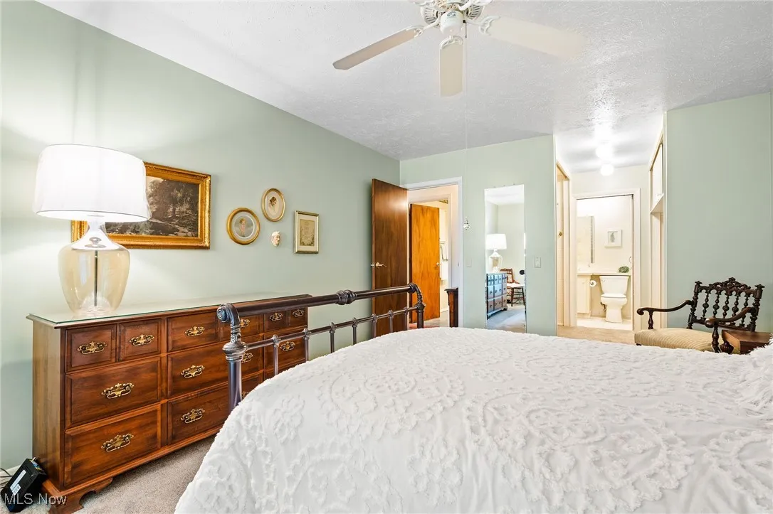 Primary bedroom featuring light carpet, ensuite bath, ceiling fan, and a textured ceiling