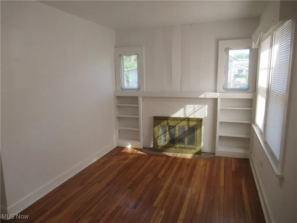 Unfurnished living room featuring dark wood-style flooring and a brick fireplace