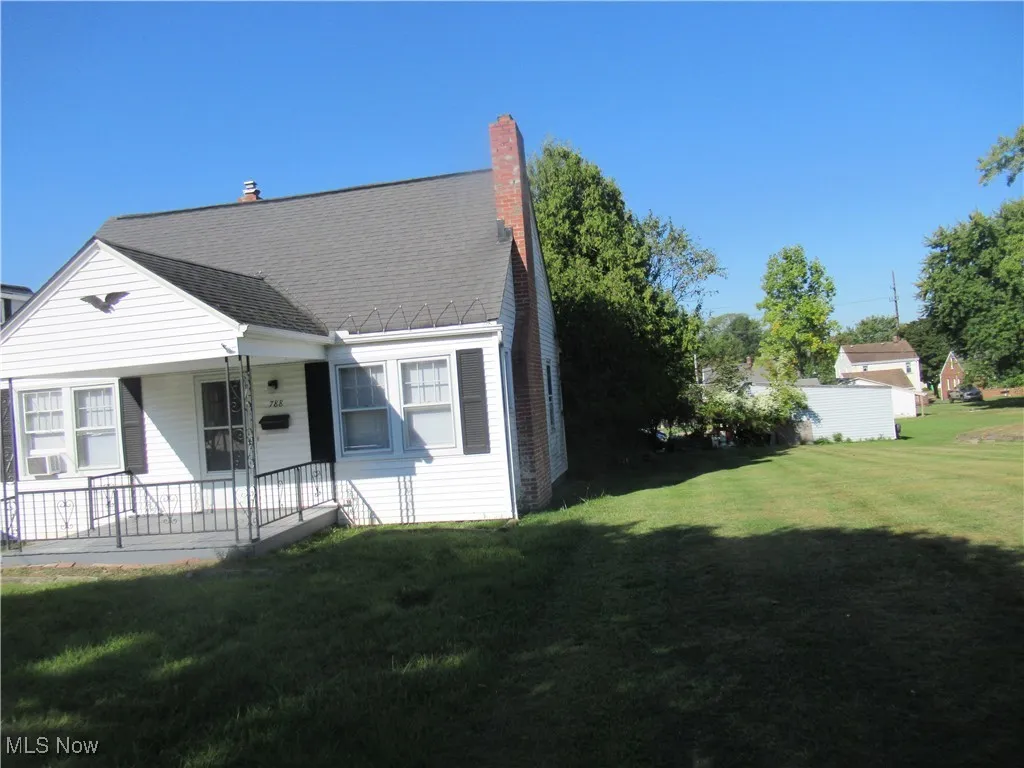 View of front facade with a front lawn, roof with shingles, a porch, and a chimney