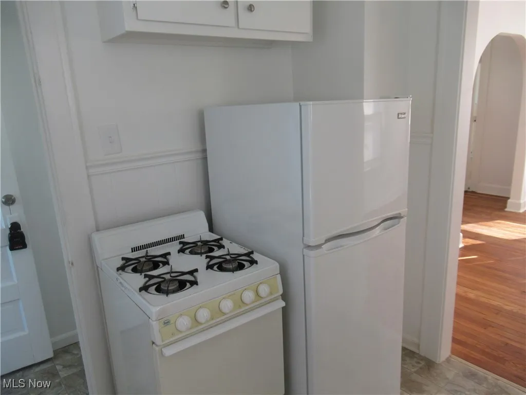 Kitchen with white appliances, arched walkways, white cabinets, and wainscoting