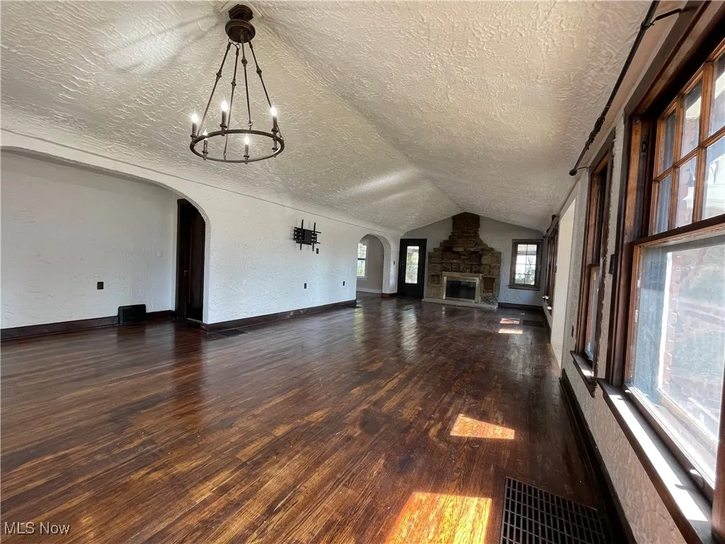 Unfurnished living room with a textured wall, lofted ceiling, arched walkways, dark wood-type flooring, and a textured ceiling