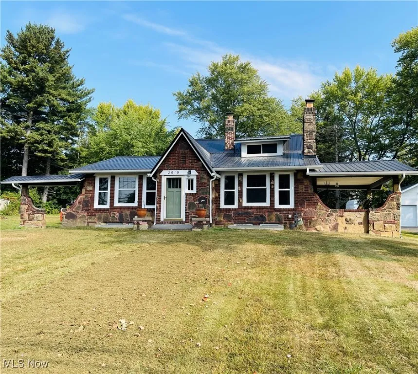 View of front of home featuring a metal roof, a chimney, a front lawn, and brick siding