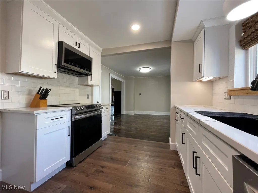 Kitchen featuring backsplash, stainless steel appliances, white cabinets, dark wood-style flooring, and light stone countertops