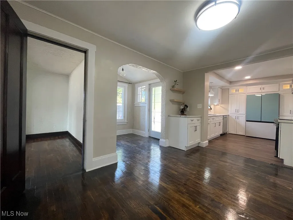 Unfurnished living room with arched walkways and dark wood-style flooring