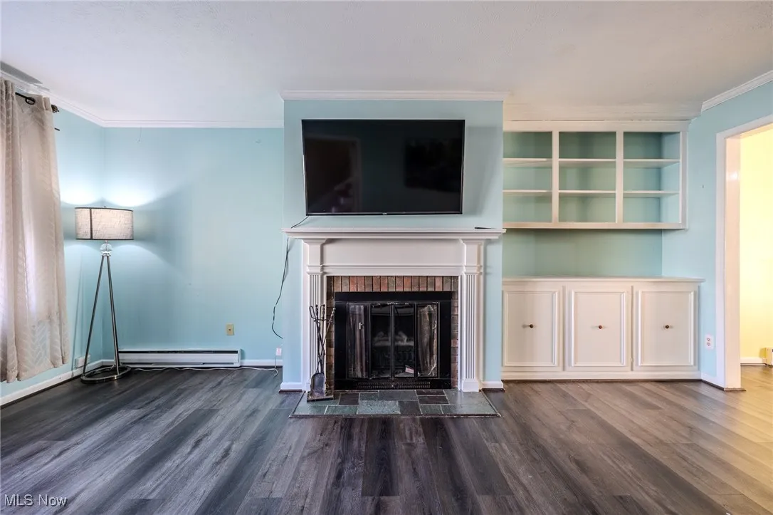 Unfurnished living room featuring crown molding, dark wood finished floors, a fireplace, and baseboard heating