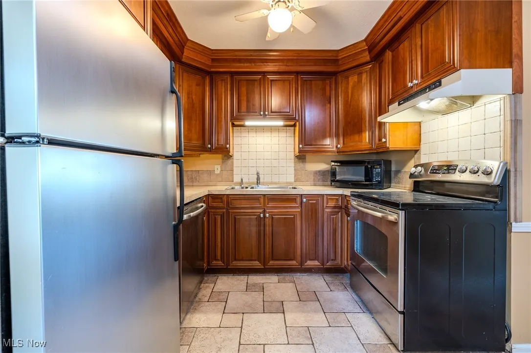 Kitchen featuring stainless steel appliances, backsplash, under cabinet range hood, ceiling fan, and light countertops