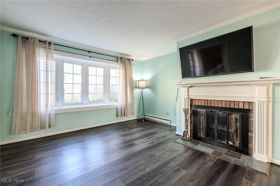 Unfurnished living room featuring ornamental molding, dark wood-style flooring, a fireplace, baseboard heating, and a textured ceiling