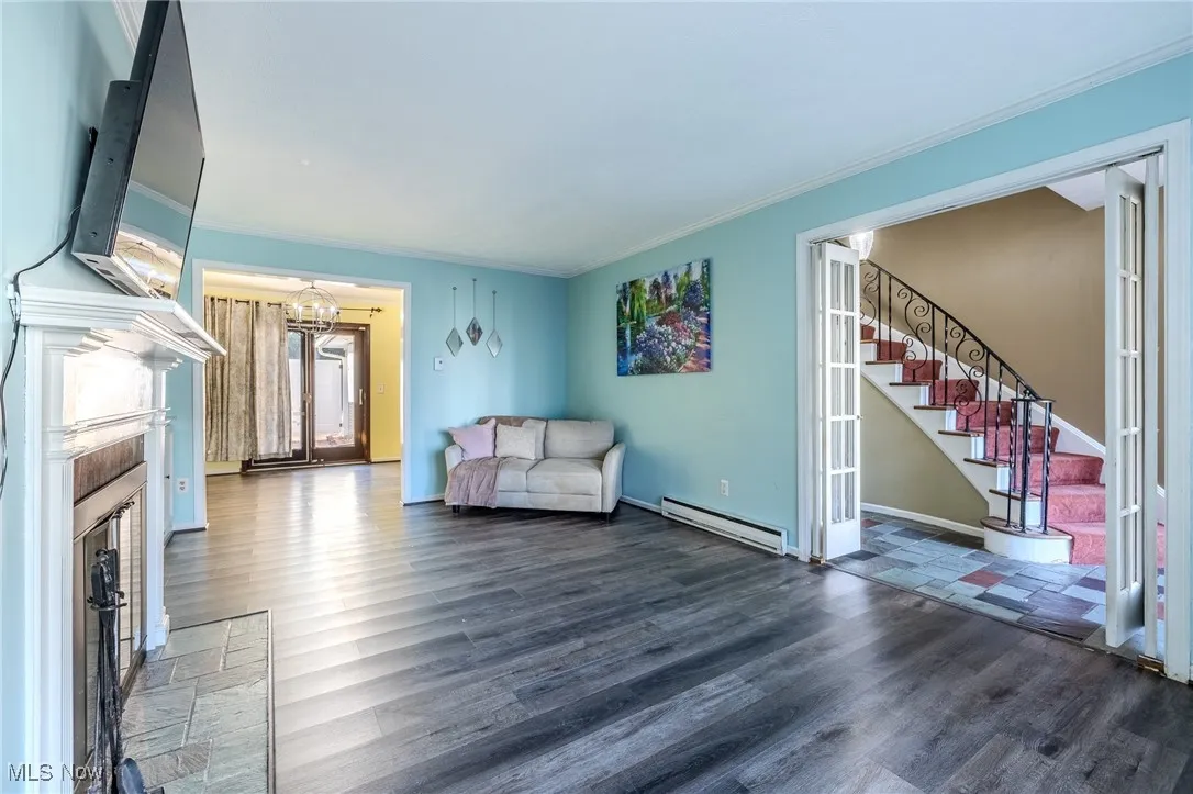 Living room featuring stairs, ornamental molding, a baseboard heating unit, dark wood-style floors, and a fireplace with flush hearth