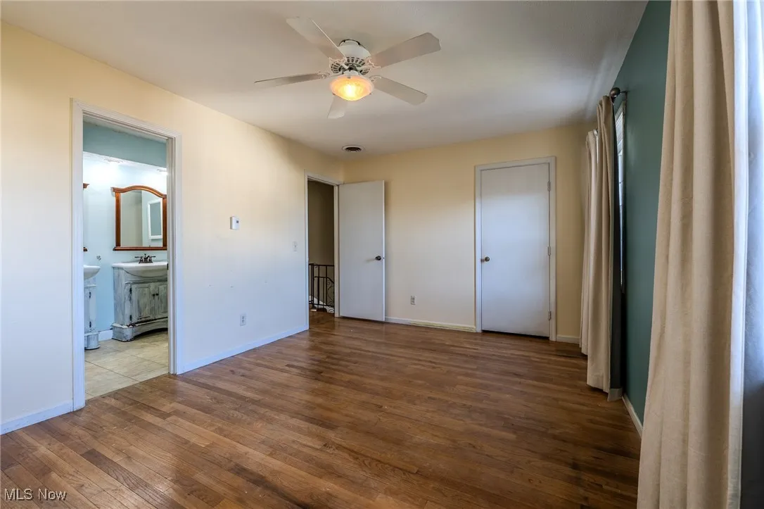 Unfurnished bedroom featuring hardwood / wood-style floors, ceiling fan, and ensuite bath