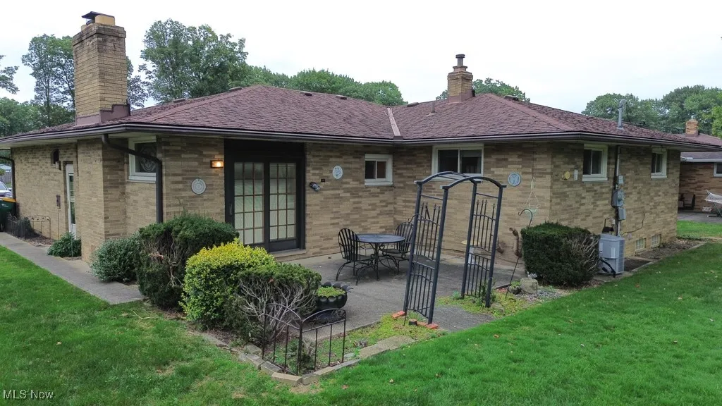 Back of house with a patio area, a chimney, a yard, and a shingled roof