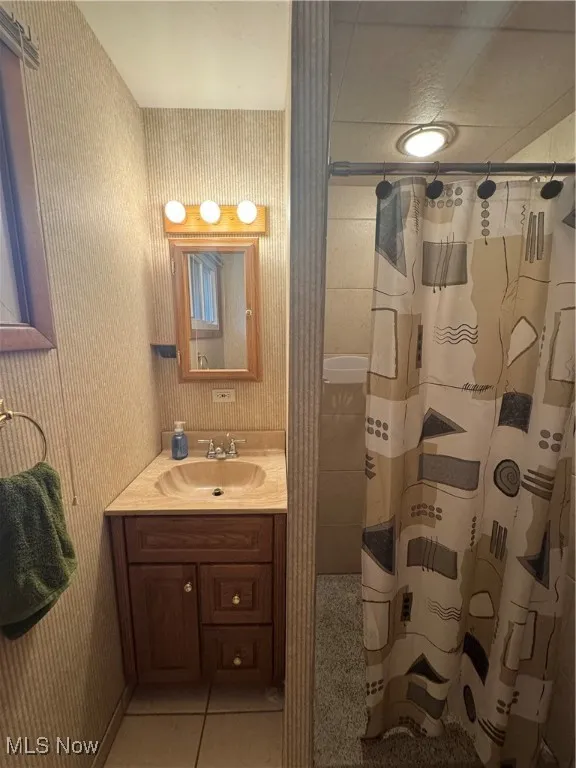Full bathroom featuring light tile patterned floors, vanity, wallpapered walls, and a shower with shower curtain