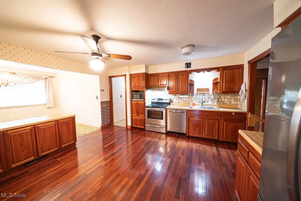 Kitchen featuring stainless steel appliances, brown cabinetry, open shelves, dark wood-style flooring, and light countertops