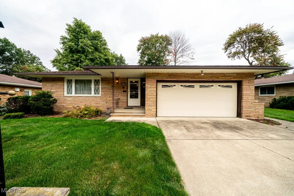 Single story home with concrete driveway, a front yard, a garage, and stone siding
