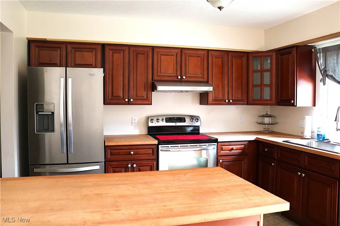 Kitchen with appliances with stainless steel finishes, under cabinet range hood, and glass insert cabinets