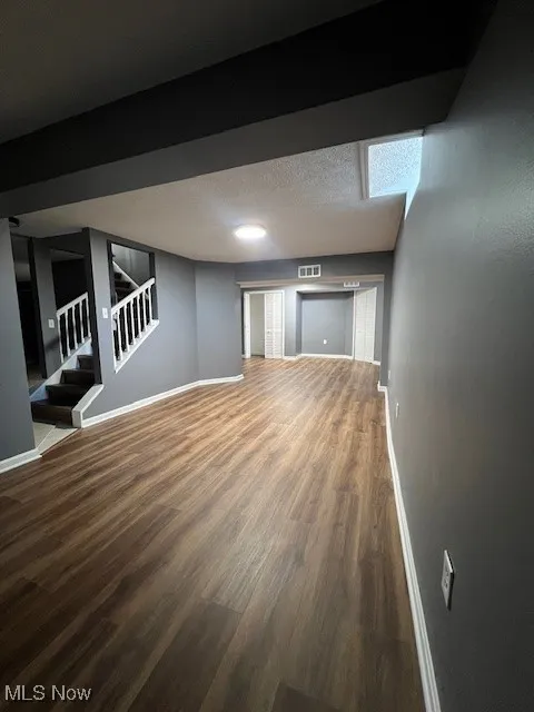 Finished below grade area with stairs, dark wood finished floors, and a textured ceiling