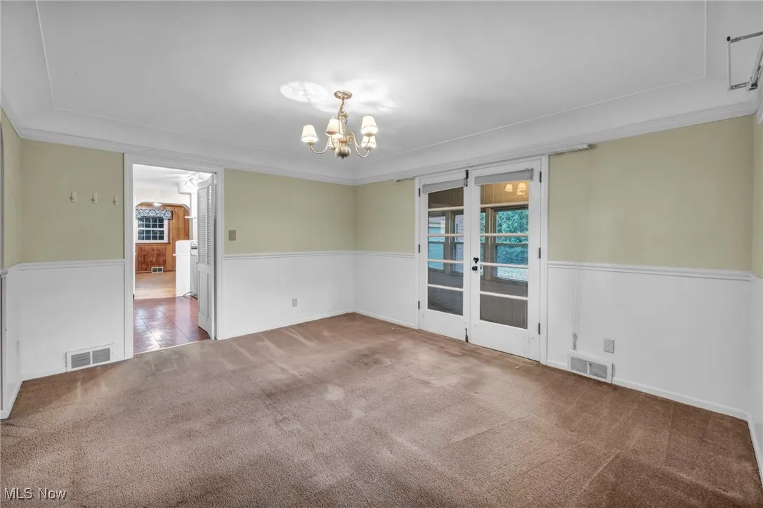 Dining area featuring french doors, carpet, crown molding, a chandelier, and wainscoting
